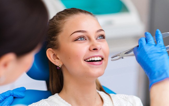 Woman smiling as dentist approaches her tooth with forceps