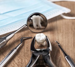 Tooth held by forceps reflected in dental mirror on wooden surface