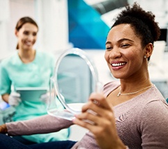 Closeup of woman smiling while looking at reflection in handheld mirror