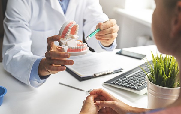 Dentist pointing to model of teeth with pen in office