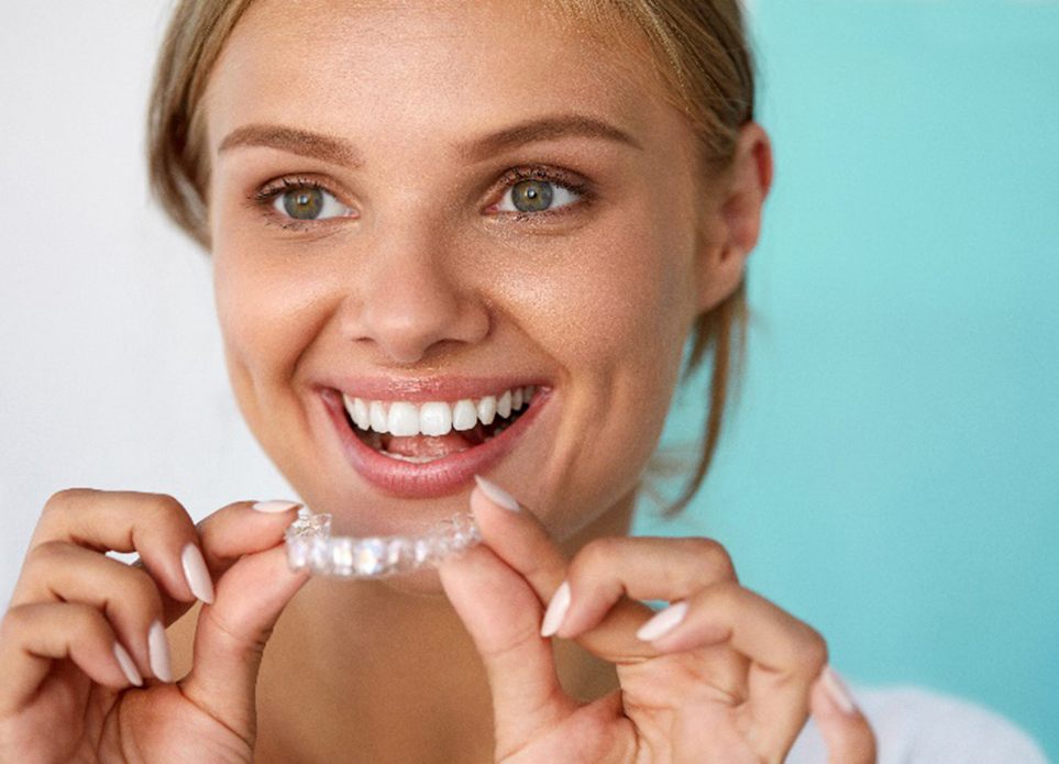 Woman smiling while holding teeth whitening tray