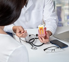 Dentist in white coat showing a model tooth to patient