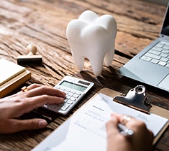 Hands calculating cost of invoice at wooden desk with large model tooth