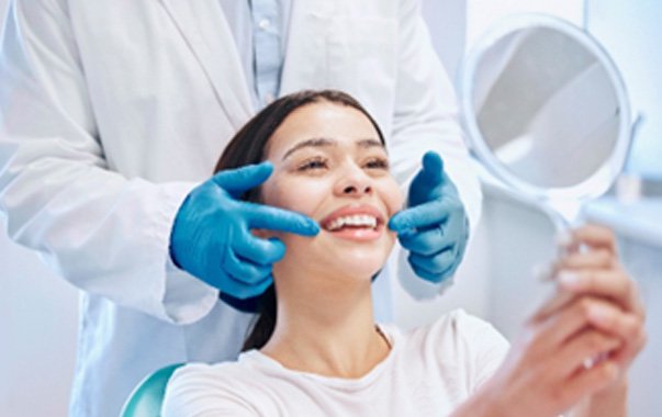 Young woman smiling at reflection in handheld dental mirror