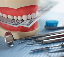 Dental model chomping down on money next to dental tools