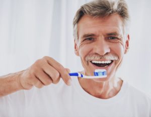 older man in white t-shirt brushing his dental implants in Spring Hill 