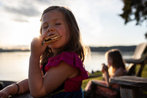 young girl enjoying s'more by lake during summer