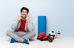 Smiling man sitting next to sports equipment and pointing to his teeth