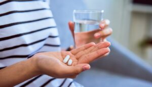 Person holding 2 pills in one hand and glass of water in the other.